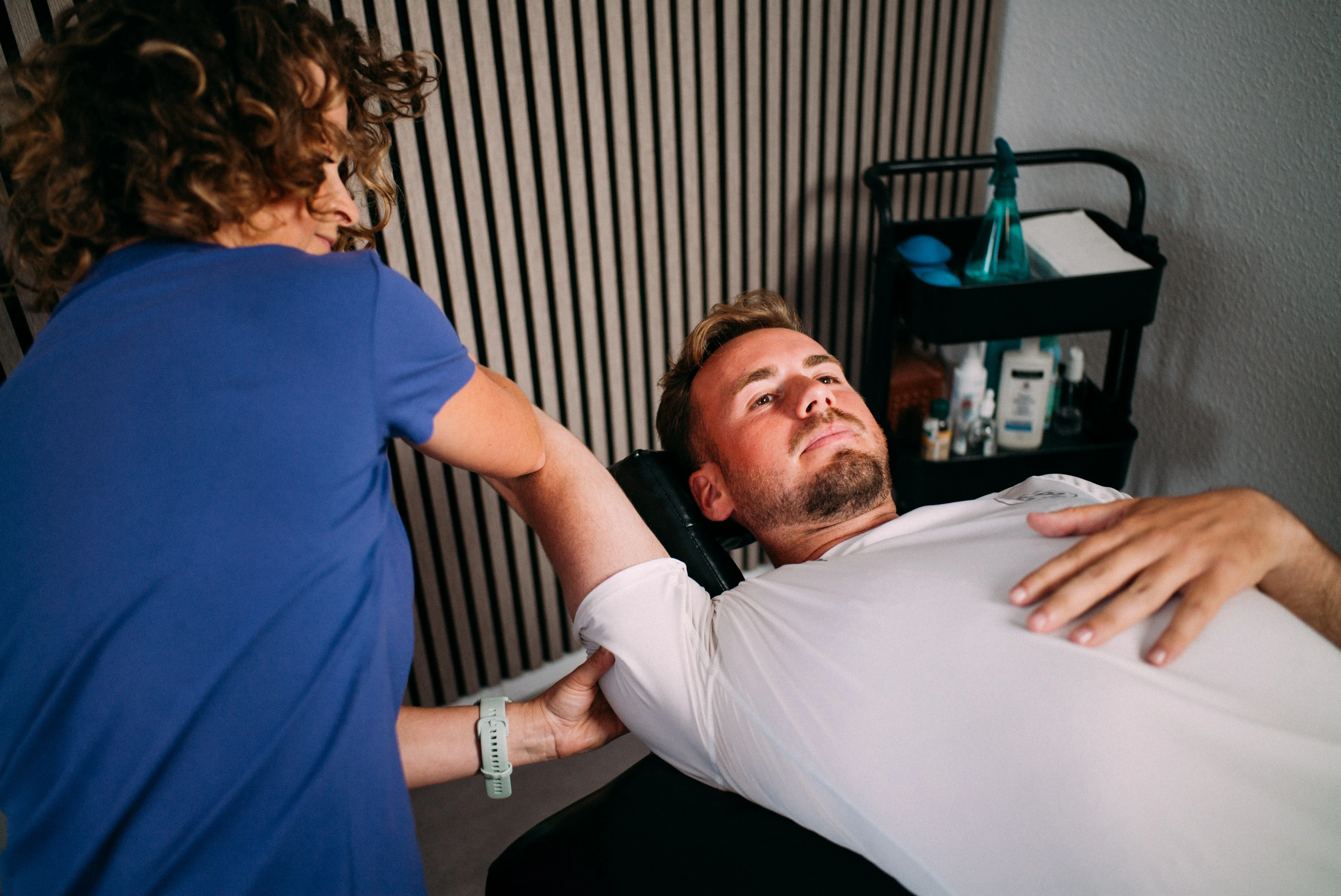Physiotherapeutin führt eine manuelle Befundung an der Schulter eines Patienten durch